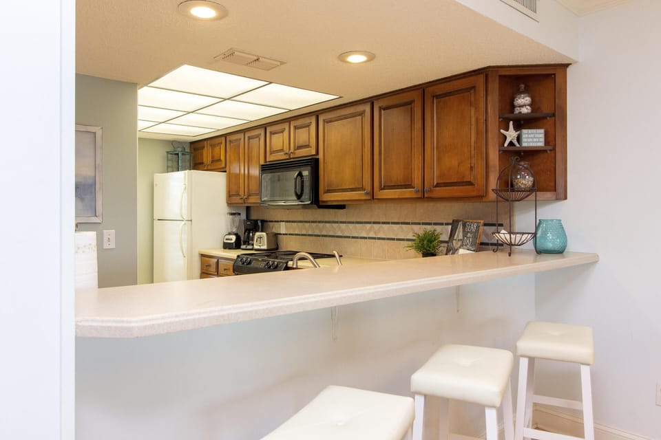 Breakfast bar with white leather stools faces beige countertop and dark wood cabinets in the kitchen.