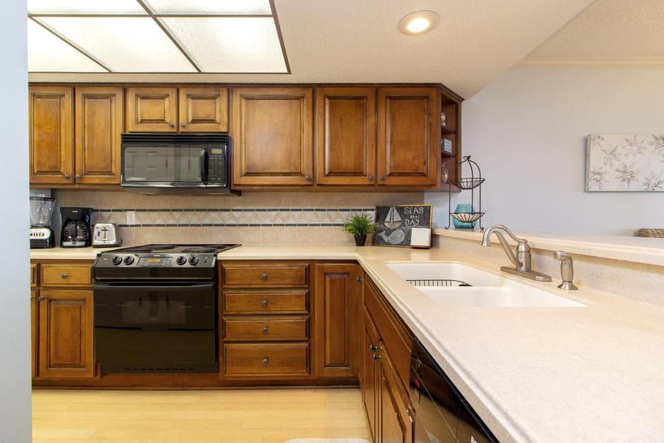 Kitchen with honey-toned wood cabinets, black appliances, beige tile backsplash, and creamy quartz countertops.