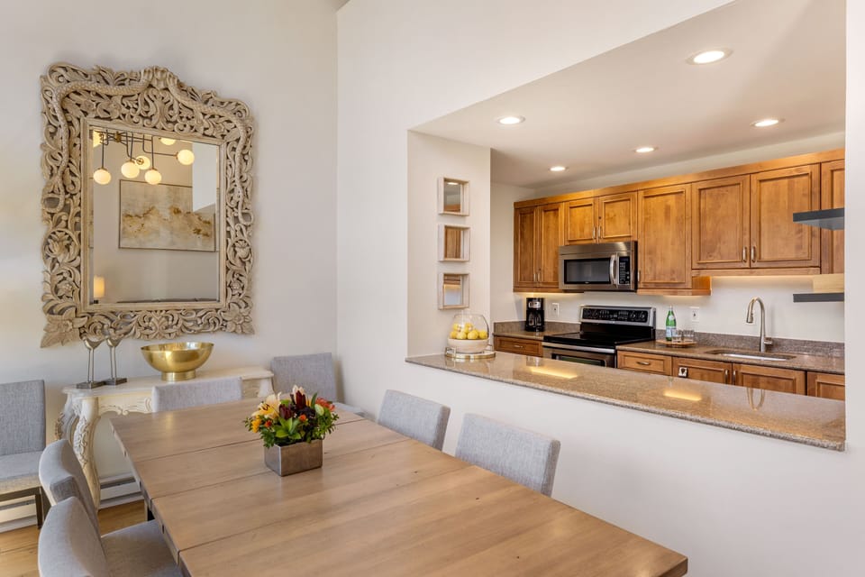 Gather around the warm wood dining table where fresh flowers welcome you home. Beyond, your fully equipped kitchen awaits with granite counters, stainless appliances, and everything you need to prepare meals together.