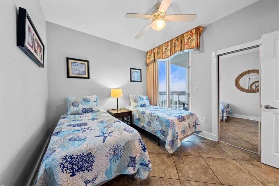 Rest peacefully in your bright guest bedroom featuring twin beds with ocean-themed linens and a ceiling fan for comfort.