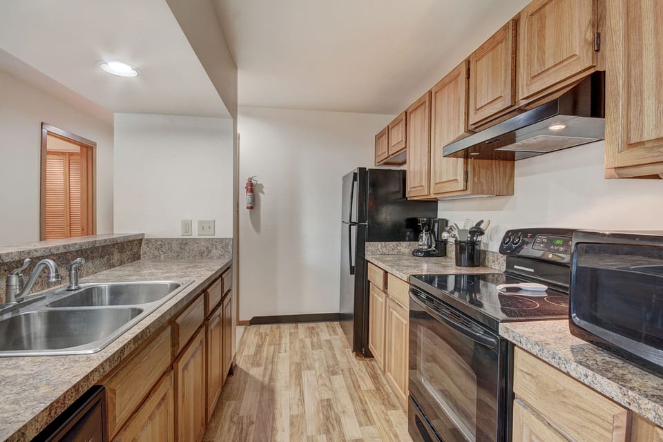 A kitchen features wooden cabinets, a black stove, black refrigerator, stainless steel sink, and a countertop with appliances including a microwave, coffeemaker, and blender.