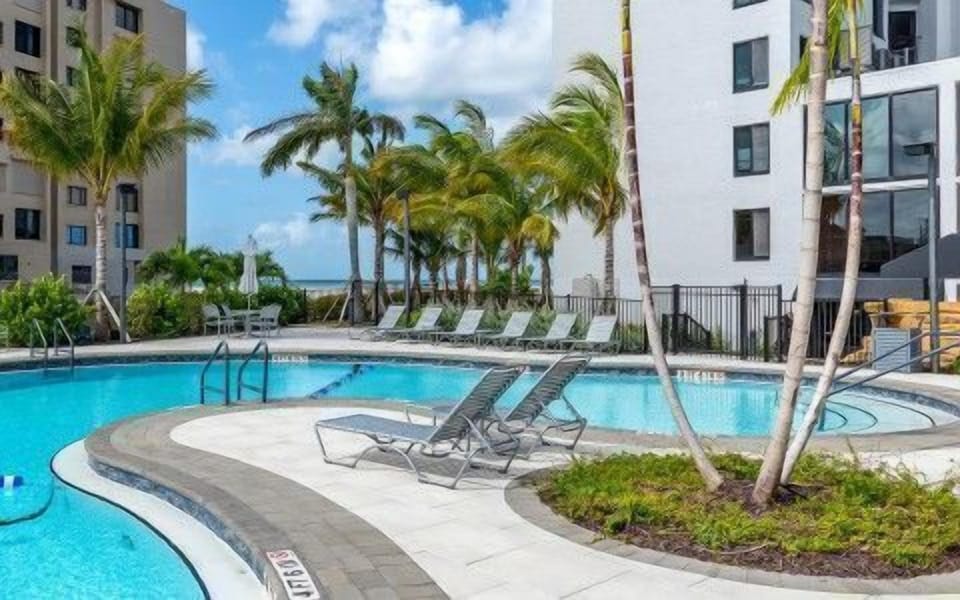 Sun-soaked lounge chairs ring the outdoor pool, framed by swaying palms and the Gulf beyond