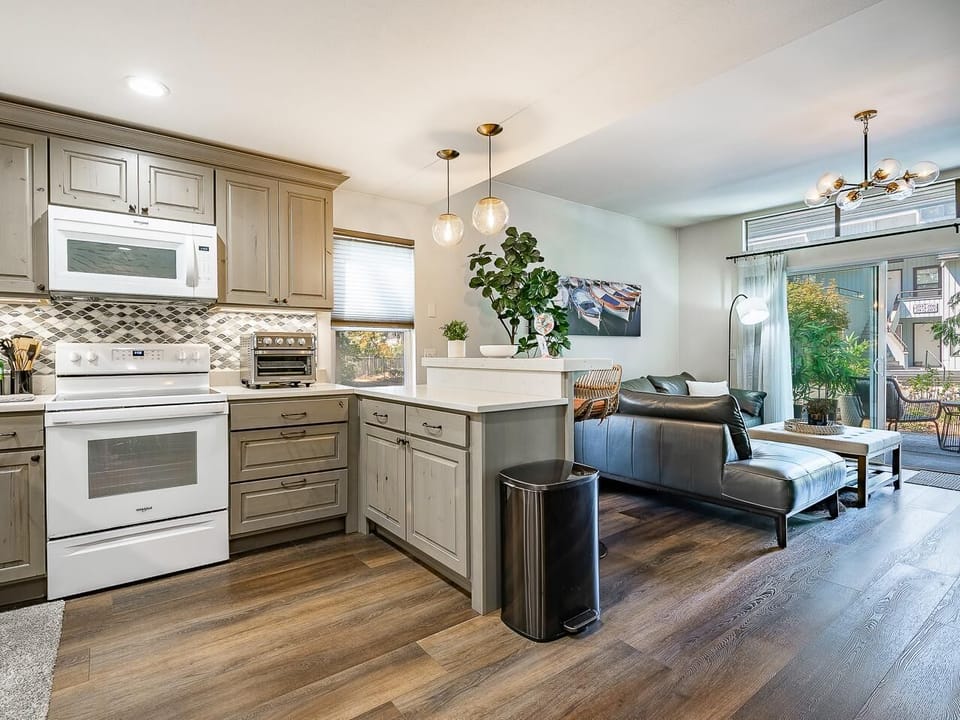 Open kitchen and living area with wood floors, gray cabinetry, white appliances, and sliding glass doors to a patio.