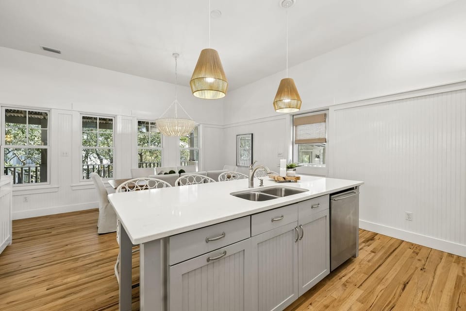 Kitchen island with quartz countertop, stainless steel sink, and pendant lights over hardwood floors.