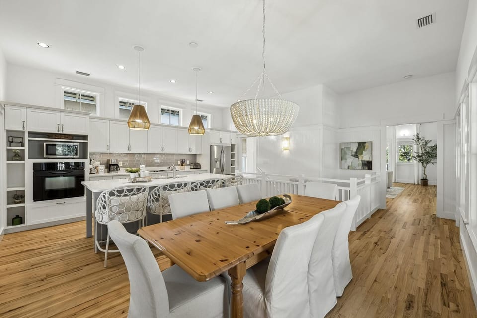 Dining area with a natural wood table, white slipcovered chairs, and a beaded chandelier overhead.