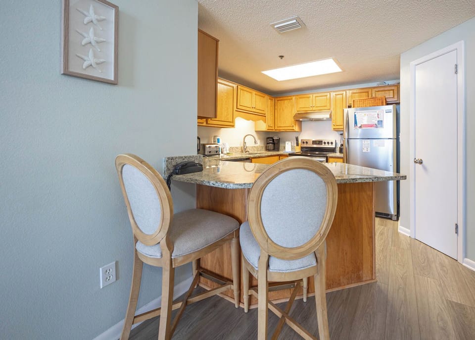 Breakfast bar with two stools complements the warm wood cabinetry and granite countertops in this inviting kitchen area