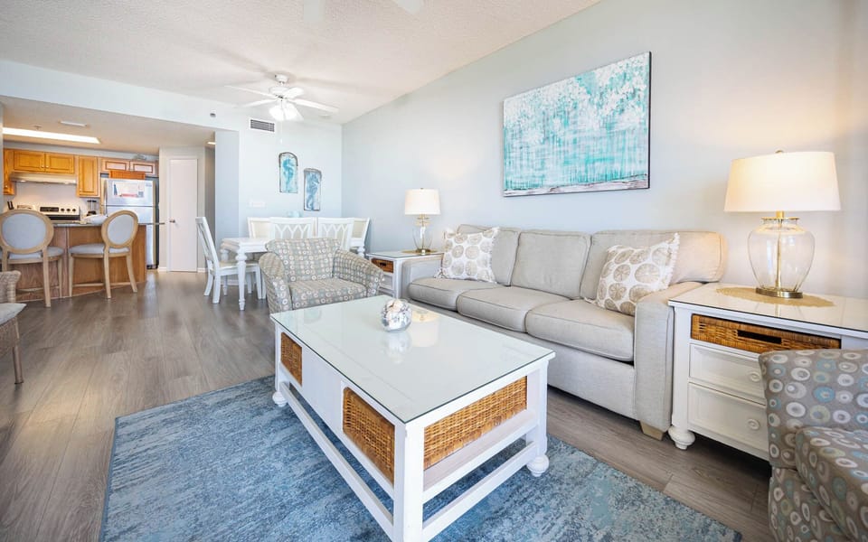 Living space features a light gray sofa, accent chair, and a glass-top coffee table, creating a welcoming atmosphere