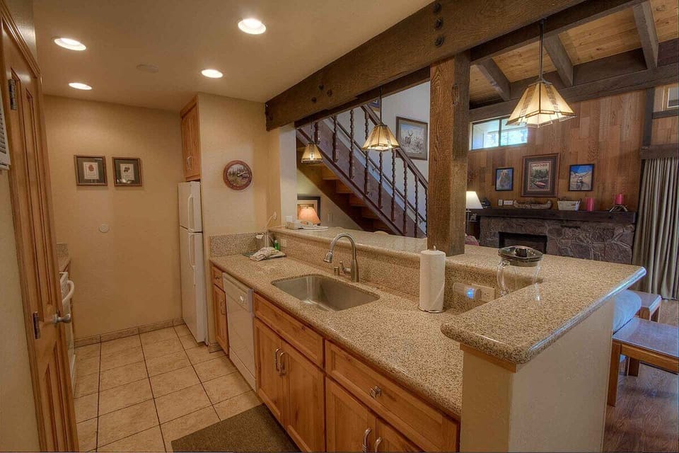 Kitchen with sink, dishwasher, refrigerator, counter space, pitcher, and living room fireplace in view.