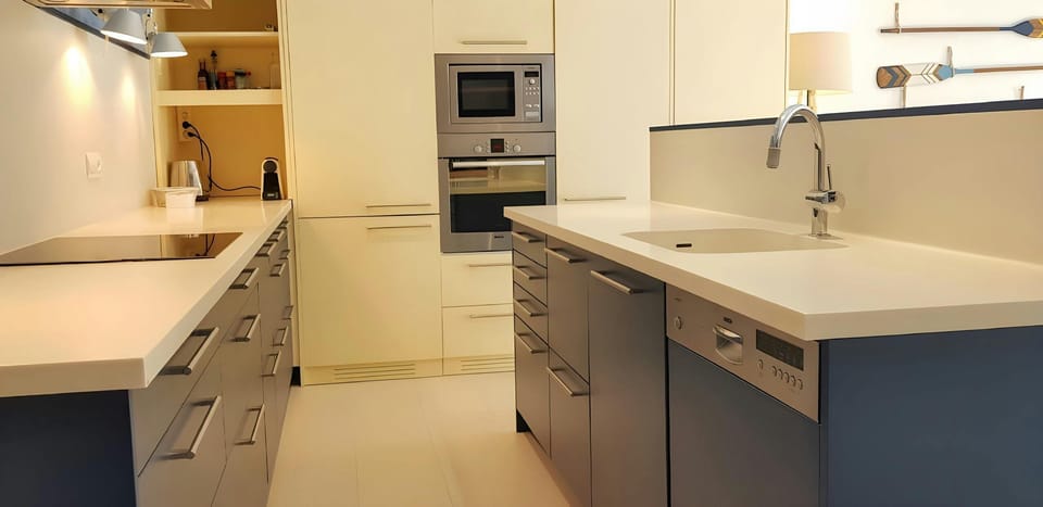 The modern kitchen features sleek, white cabinetry and stainless steel appliances, including an oven, microwave, and dishwasher. This spacious kitchen provides ample room for meal preparation and entertaining.  The open floor plan connects the kitchen wit