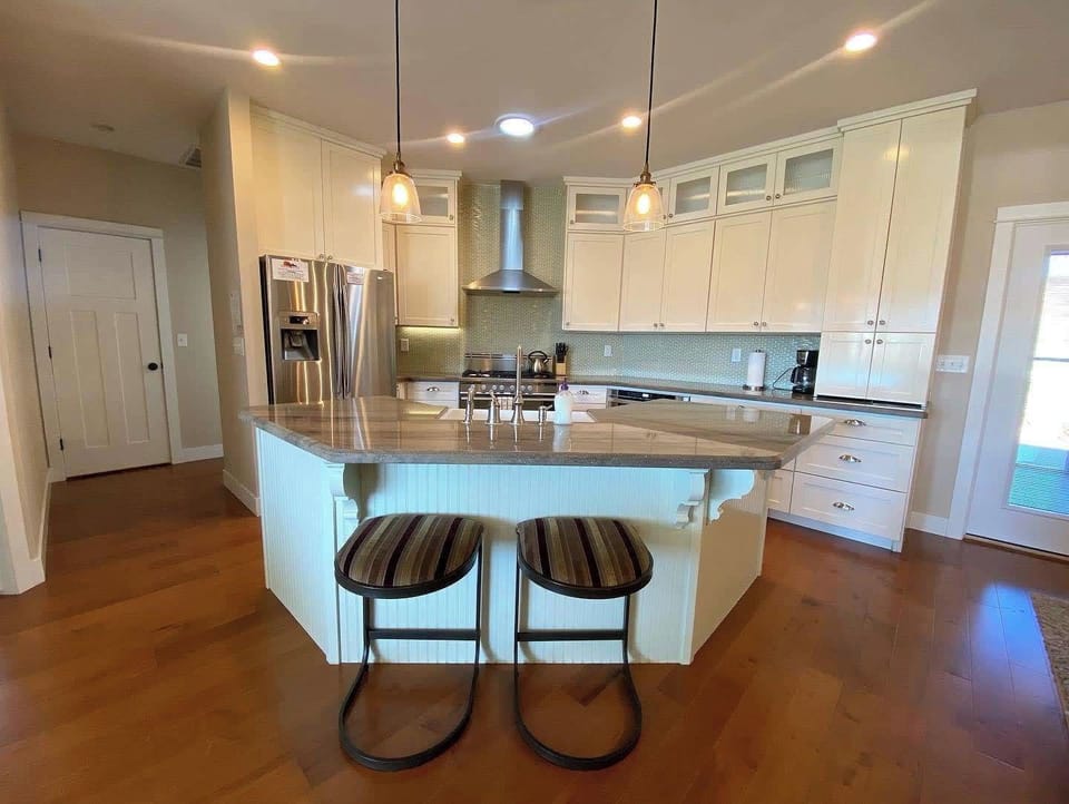 Bright white kitchen with a spacious granite island and seating for two at Midnight Manor, Kanab.