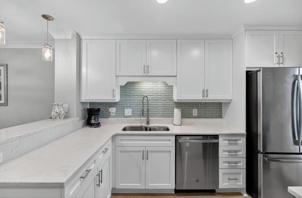 Your gourmet kitchen awaits with gleaming marble countertops, stainless steel appliances, and a soothing seafoam glass-tile backsplash—perfect for preparing your favorite meals in style.