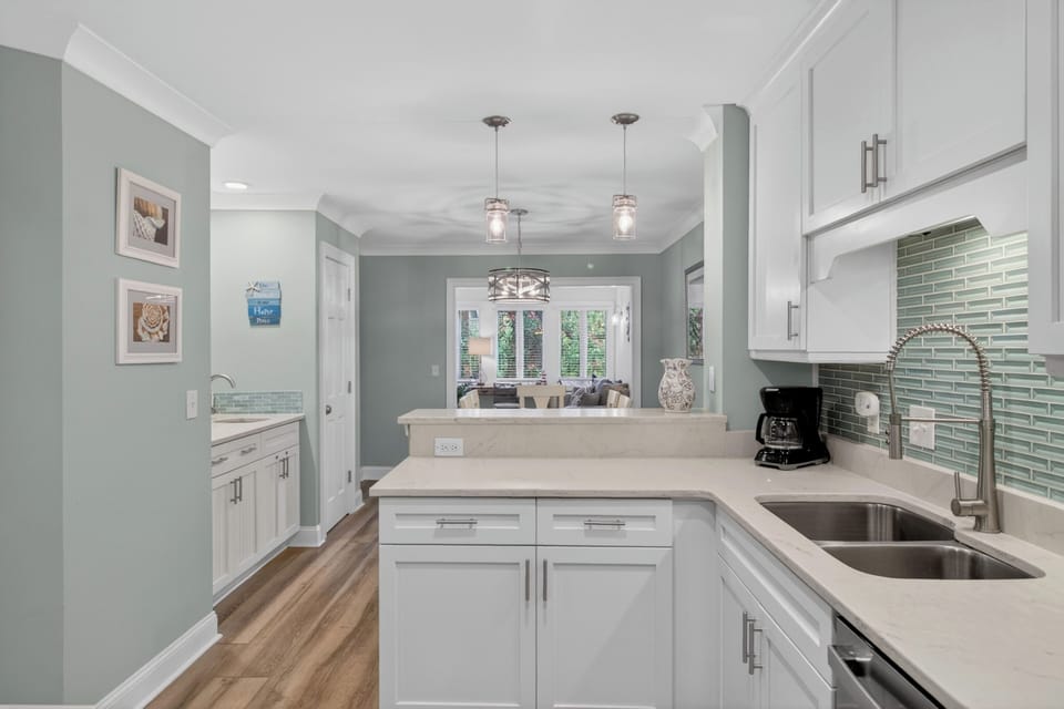 Step into a bright, coastal-inspired kitchen where your mornings unfold beneath charming pendant lights. Gleaming quartz counters, crisp cabinetry, and sea-glass tile invite you to gather, cook, and unwind in effortless style.