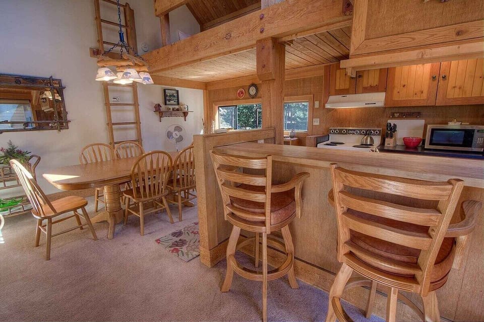 Breakfast bar with chairs beside a dining table set for six, with a range, microwave, and cabinets.