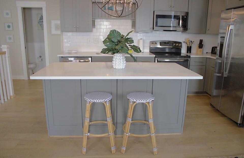 The upstairs kitchen features a modern, coastal-inspired design with gray cabinetry, white quartz countertops, and a white subway tile backsplash.