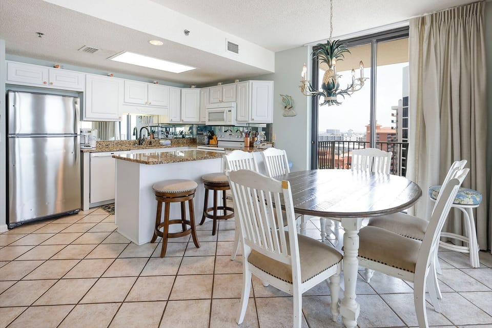 Bright dining area features a round table with white chairs and a cozy breakfast bar, complemented by a view of the balcony