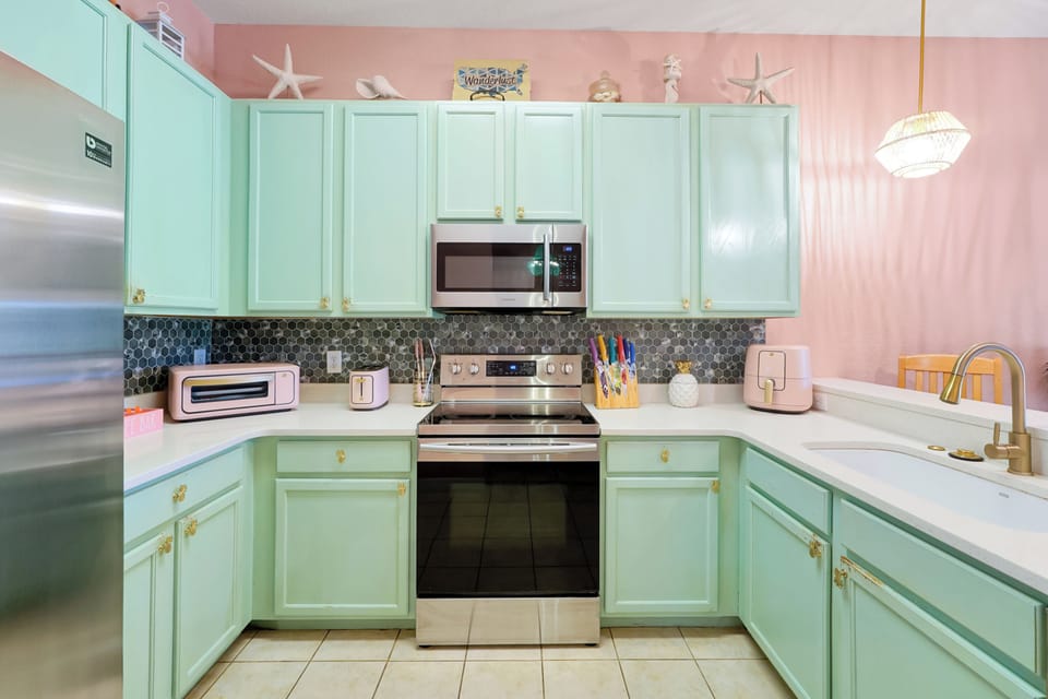 Bright, tropical kitchen featuring quartz countertops, green cabinetry, and a fun splash of pink — island vibes all around!