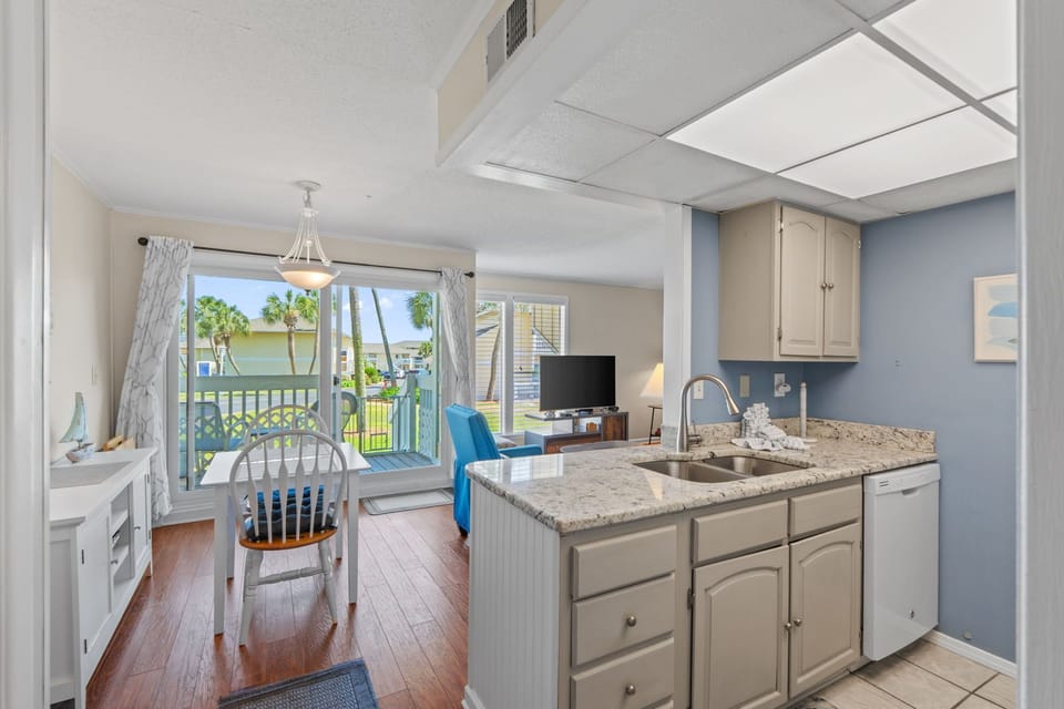 Your open-concept kitchen flows seamlessly into the living area, with granite counters and a view of swaying palms through the balcony doors.