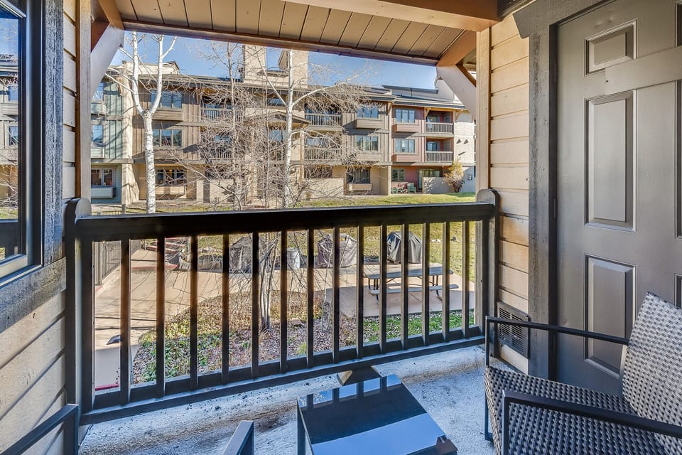View from a covered balcony with outdoor furniture overlooking a courtyard area with BBQ grills and other residential buildings.