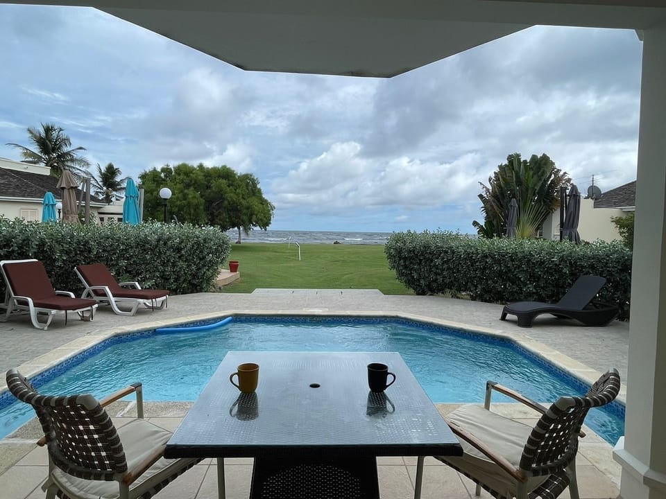 Expansive ocean-view patio with 4 seater dining set, pool ad lounging chairs.