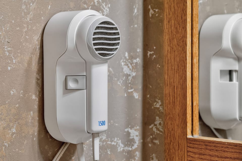 Wall-mounted hairdryer ready for your use, with a mirror close by for easy styling and grooming.