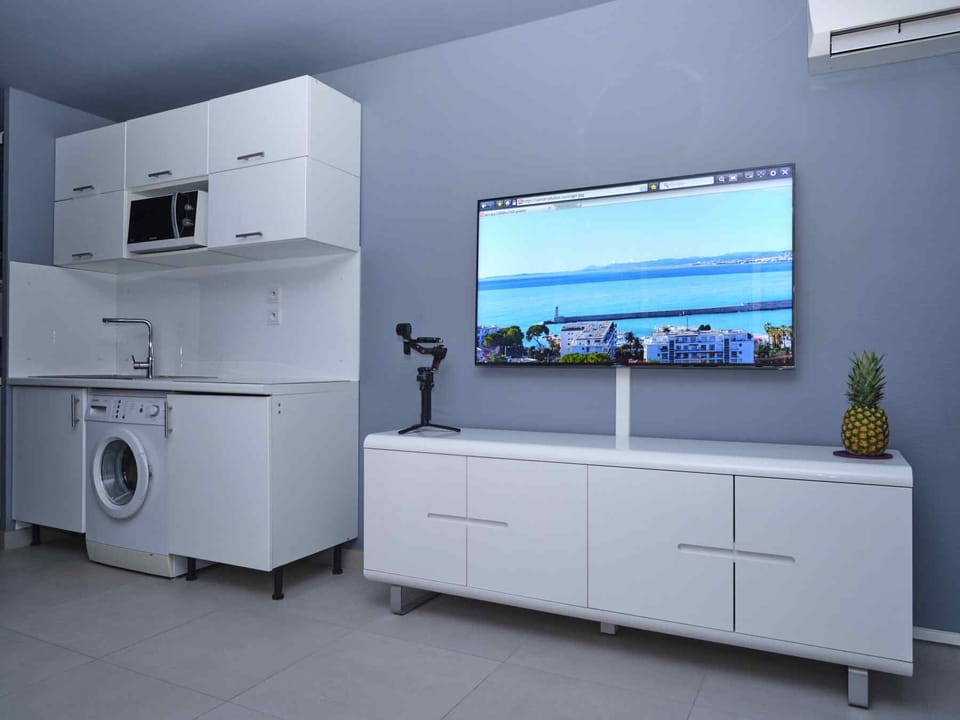 The TV and kitchen with a washing machine and a microwave oven.