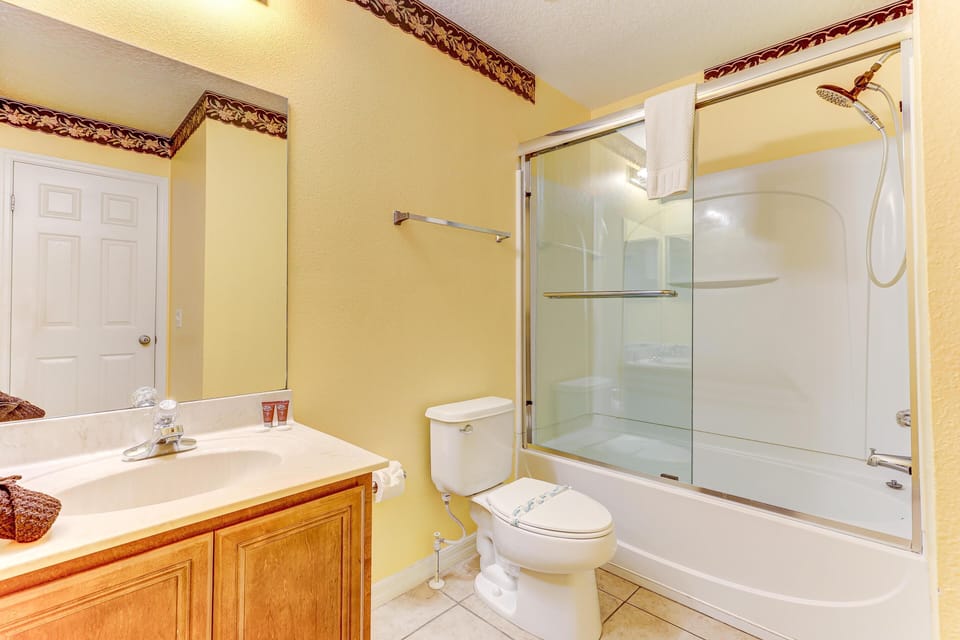 Bathroom features a wood vanity with marble countertop, white toilet, and a tub-shower combo with sliding glass doors.