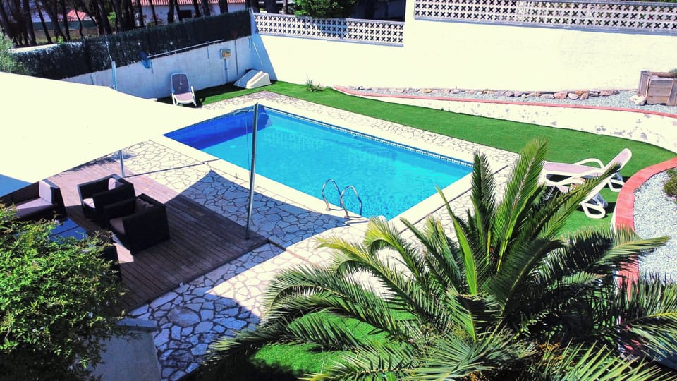 Dive into the sparkling private pool. A shaded outdoor lounge provides cool comfort amidst lush palms and sunlit terraces.