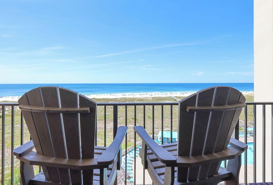 Adirondack chairs on the balcony overlook the beach and sparkling gulf waters, inviting relaxation and enjoyment of the view