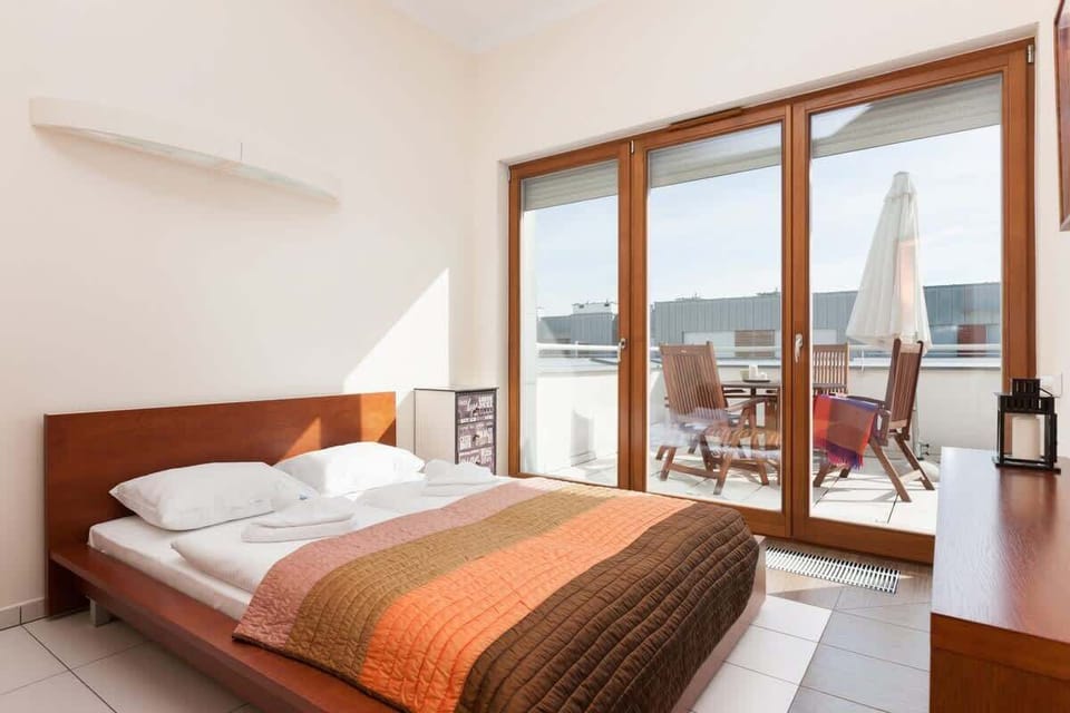 A cozy bedroom with a double bed, decorated in warm tones, and access to a spacious terrace through large glass doors.