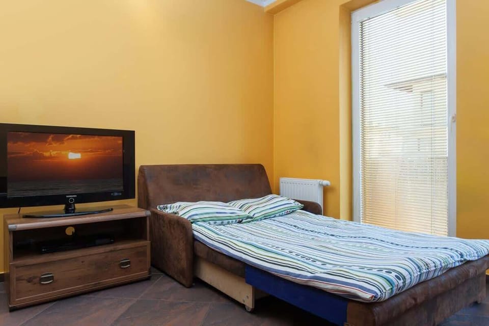 The living room’s seating area with a sofa and armchair, positioned around a TV. The cozy seating setup is complemented by the yellow wall, creating a welcoming environment.