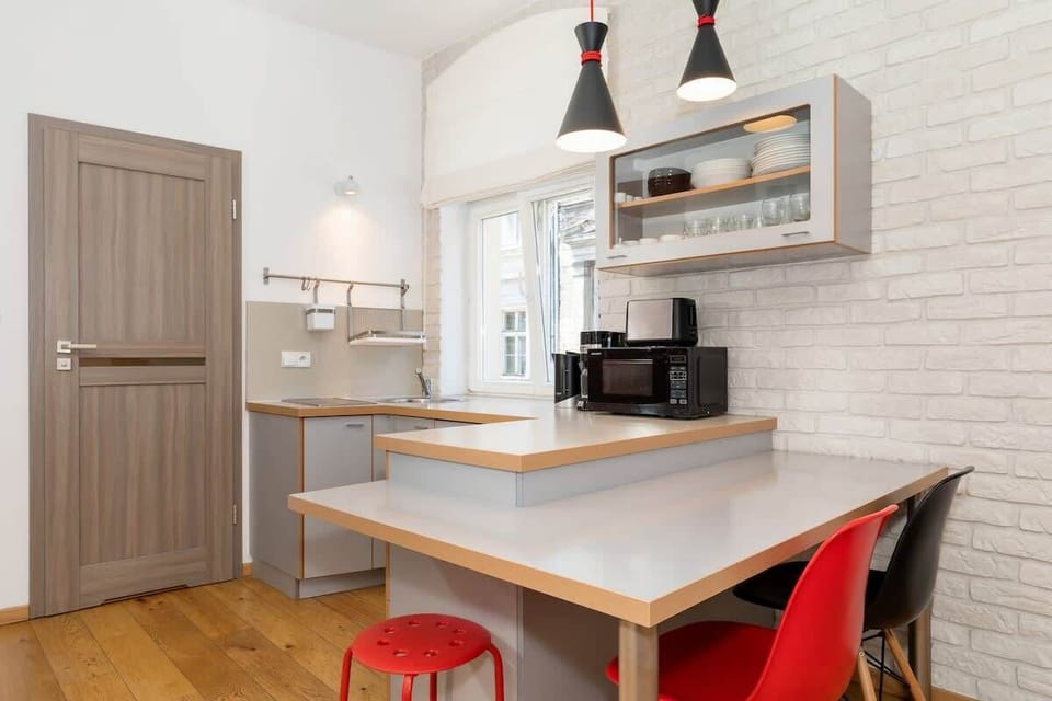A compact kitchen with grey cabinetry and a white backsplash. The small dining area next to the kitchen includes bar-style seating, perfect for quick meals.