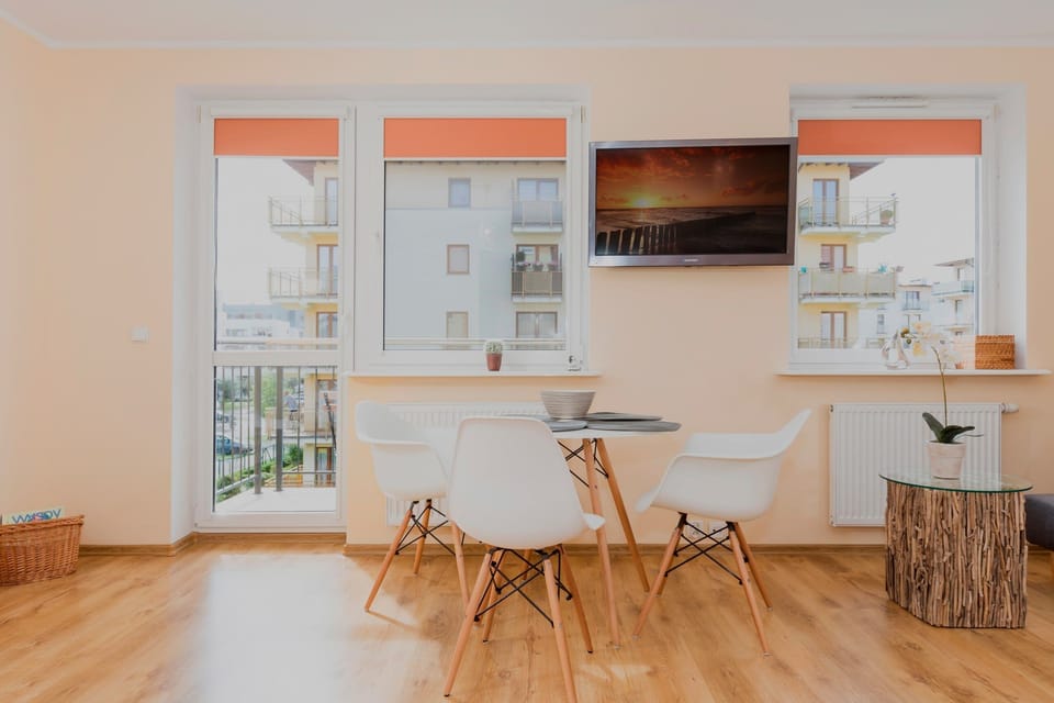 A compact dining area near large windows. The round table has two white chairs and offers a cozy space for meals with plenty of daylight.