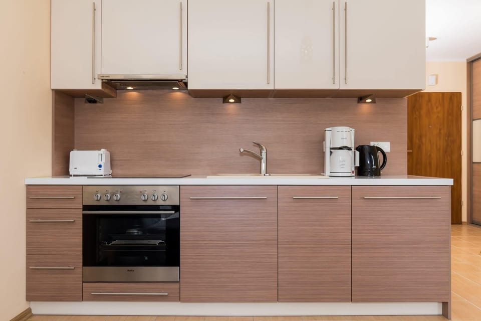 A close-up of the kitchen area, showing wooden cabinets, a built-in oven, and basic appliances. The space is well-organized and minimalistic.