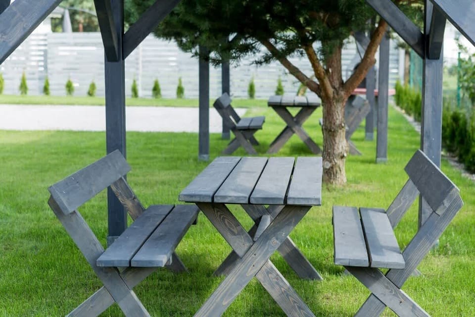 An outdoor seating area with wooden benches and a gazebo, providing a shaded space for relaxation and dining, set in a well-maintained garden with lush greenery.