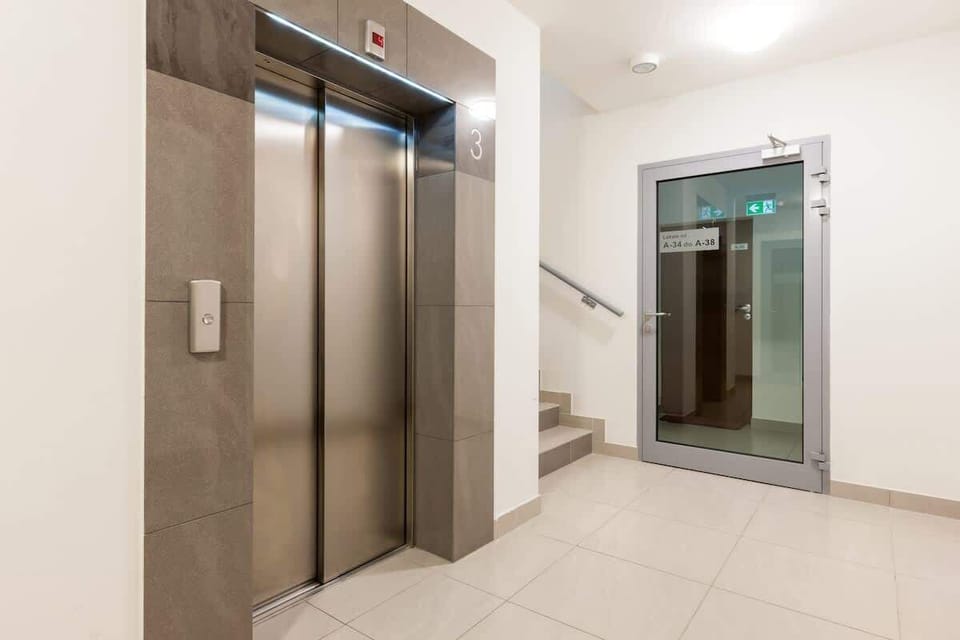 A hallway or lobby featuring a pair of elevators and light-colored tile flooring. The space is well-lit, and the elevators seem to provide easy access to different floors.