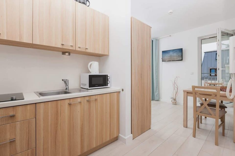 A small kitchen setup with wooden cabinets and a compact dining area. The kitchenette includes modern appliances, and the table provides a cozy space for meals.


