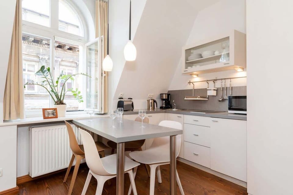 A bright, modern kitchen with white cabinets, a dining table, and a unique combination of pendant lights hanging above. The space has a clean and minimalist design.