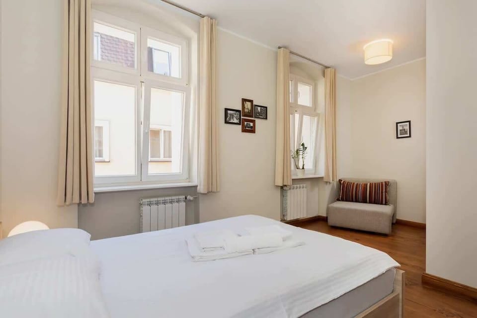 A spacious bedroom featuring a double bed with white linens and a large window that brings in lots of natural light. The wooden floor adds warmth to the room.