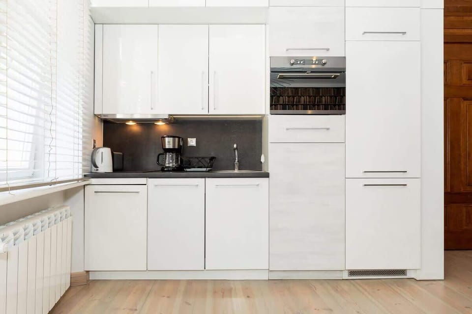 A bright kitchen with white cabinets and modern appliances. The space is simple, functional, and well-lit by a window.