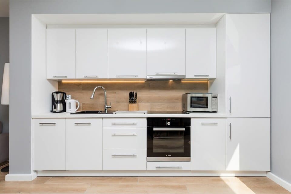 A stylish kitchen with white cabinetry and wood countertops, leading into an open-plan living area with elegant decor and modern lighting.