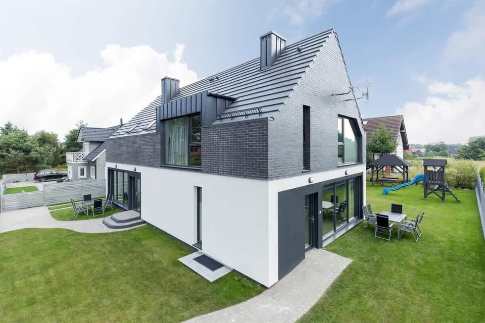 The exterior of a modern home with a gray and white facade, well-maintained greenery, and a spacious outdoor seating area, giving a clean and elegant appearance.