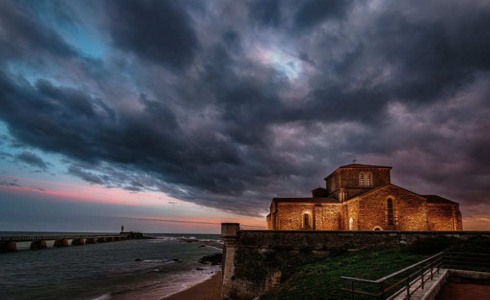 A historic stone building standing beneath a moody sky of dark, swirling storm clouds at dusk.