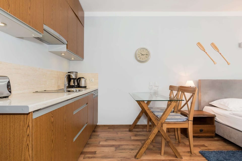 The kitchenette area in the studio features wooden cabinets and an adjacent dining space with a small table and chairs. It provides everything needed for cooking and eating in a compact layout.