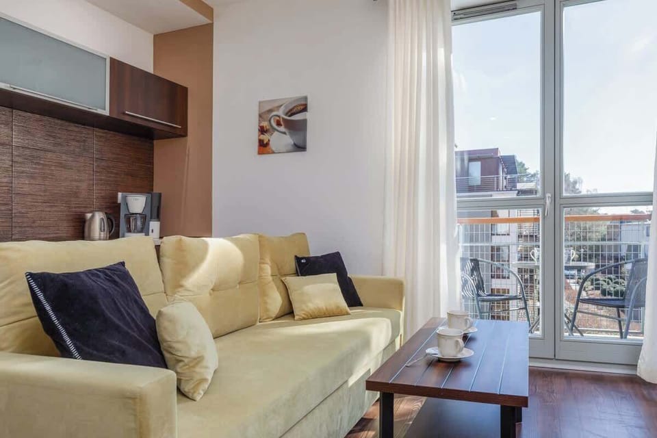 A living room with access to the balcony, featuring cream-colored seating and accent cushions, providing a cozy and airy atmosphere.
