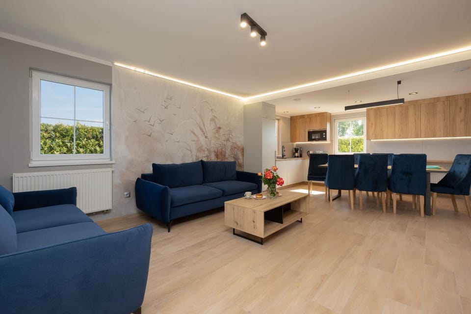 A modern living room featuring a spacious blue sectional sofa, wooden coffee table, and large windows that flood the space with natural light, creating an inviting and airy atmosphere.