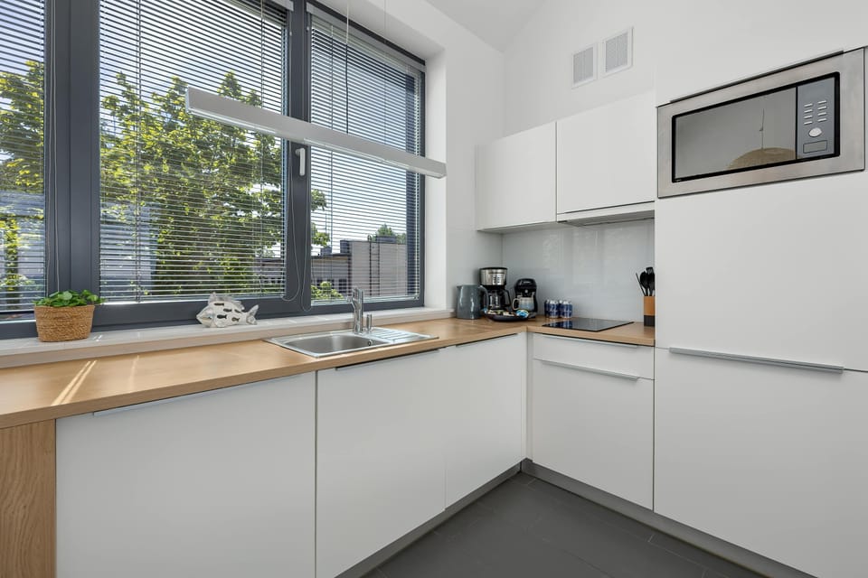 A clean, L-shaped kitchen area showcases minimalist white handleless cabinetry and a warm wood-toned countertop. A built-in microwave and integrated appliances make excellent use of the compact space.