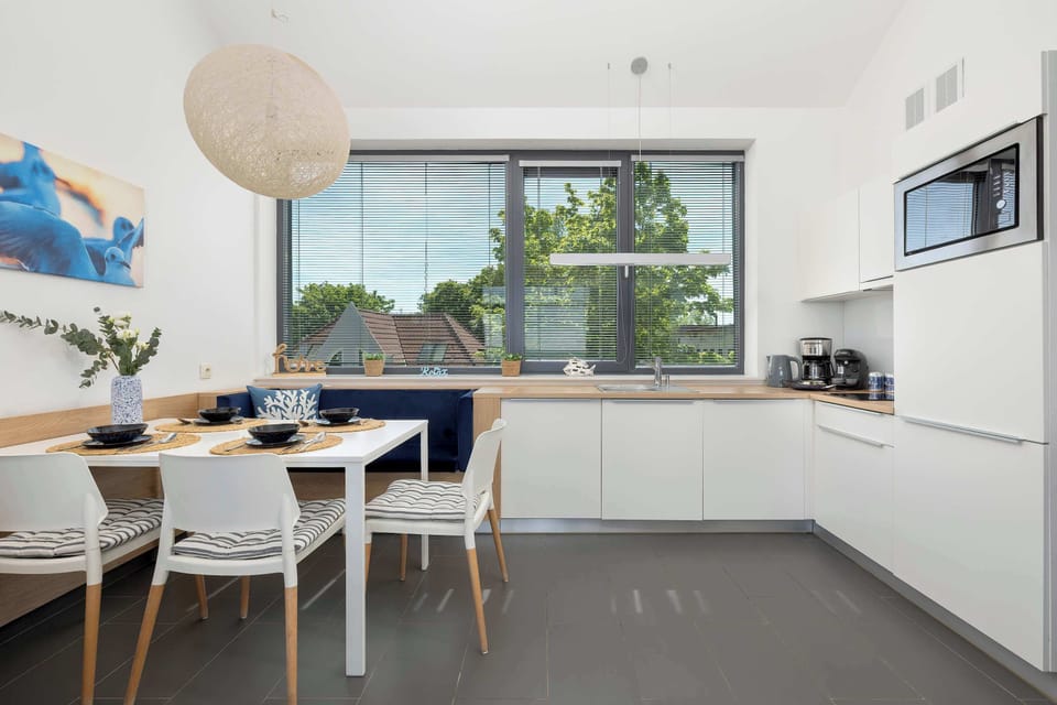 The open kitchen and dining area are captured from a straight-on perspective, highlighting the uniform white theme. An abstract blue canvas painting adds a vibrant splash of color to the dining nook wall.