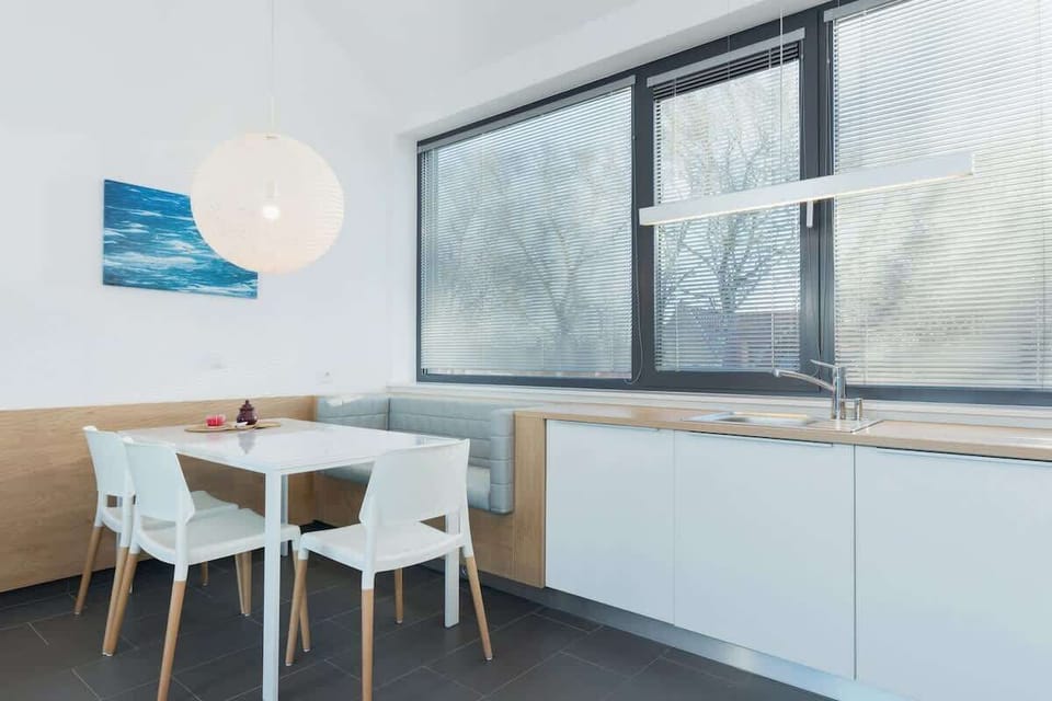 A bright kitchen with white cabinets and a dining table for four. The large windows allow light to flow through and reveal the sea outside.