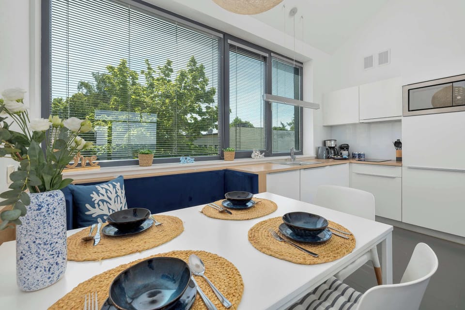The dining layout is presented from a lower perspective, emphasizing the contrast between the white tabletop and the blue upholstered bench. A glass vase holding delicate flowers serves as a simple centerpiece.