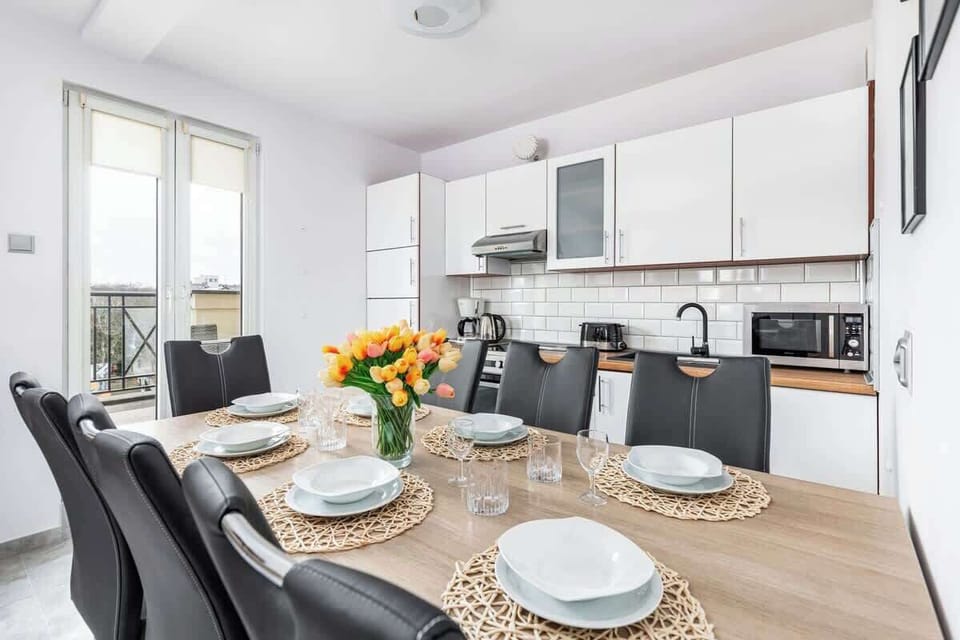 A modern, white kitchen with a small window, sleek cabinetry, and stainless steel appliances. The space is compact but efficient for cooking and dining.